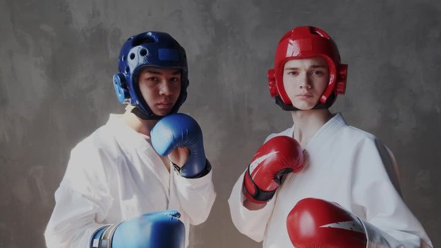 Two resolute and aggressive guys in defense helmet and fight box gloves looks into the camera and ready for action. Face of young focused sportsman before championship.