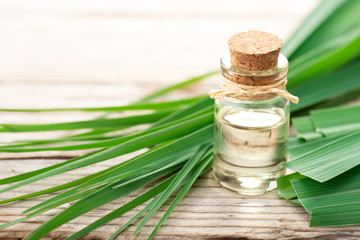 lemongrass essential oil in the bottle, with fresh lemongrass leaves, on the wooden table