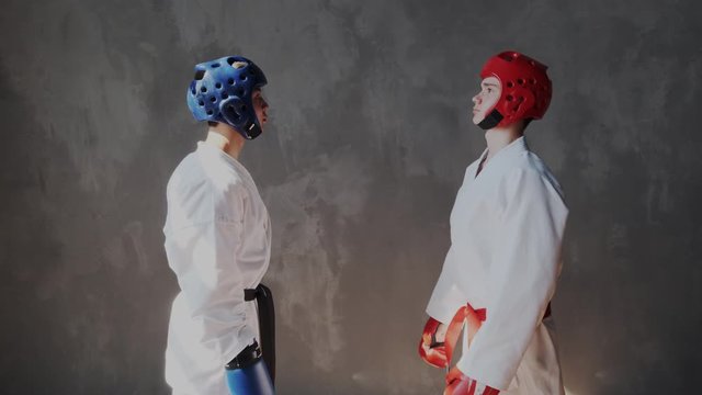 Two young strong teens in protective helmet and fight box gloves warm up muscles, take a fighting stance and looking into the lens. Camera zoom in to concentrated sportsmans.