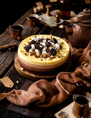 Beautiful still life with homemade delicious three chocolates cheese cake on wooden stand on rustic table