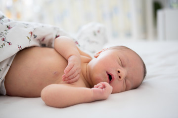 Beautiful newborn baby boy in bed. Infant lying down in bed