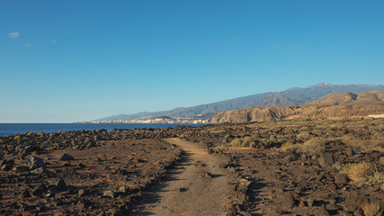 Arid volcanic landscape of Malpais de la Rasca, a natural reserve close to Palm-Mar town, with views towards Atlantic Ocean and the tourist resort Los Cristianos, in Tenerife, Canary Islands, Spain