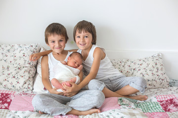 Two children, toddler and his big brother, hugging and kissing their newborn baby brother at home