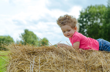 Naklejka na ściany i meble children's games on a round haystack during the harvest and harvesting of wheat. Summer sunny day. German child sitting on hay bale during Oktoberfest. soft focus.