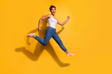 Fototapeta na wymiar Full length side profile body size photo funny she her dark skin model lady jumping high champion rush sale discount shop wear casual jeans denim pants trousers tank-top isolated yellow background