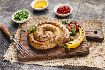 Grilled chili and spiral sausage on wooden cutting board near bowl of ingredient