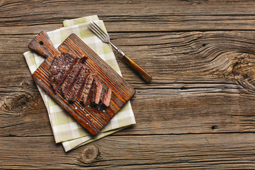 Slice of grilled steak on cutting board with fork and napkin over table