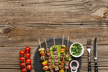 Hot grilled kebab skewers with vegetable on black slate over wooden surface