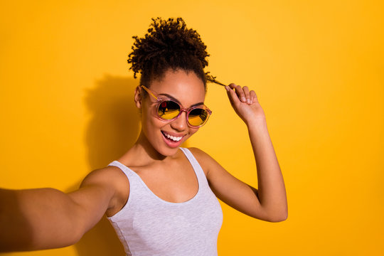 Close up photo beautiful nice pretty she her dark skin lady summer weekend rest relax make take selfies blogger play fingers wind curl wear sun specs casual tank-top isolated bright yellow background