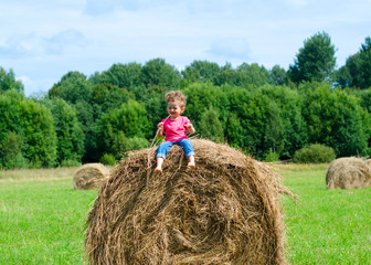 Naklejka na ściany i meble Cute kid girl in glasses and fashion clothes sit on the round hay bale in countryside in wheat field. harvest time in Germany.Celebrating Oktoberfest. soft focus.
