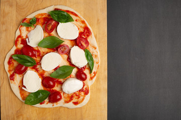 Uncooked homemade pizza on cutting board on dark background