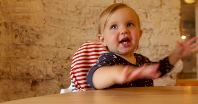 Joyful adorable kid playing with hands at wooden table waiting food in cozy cafe cozy