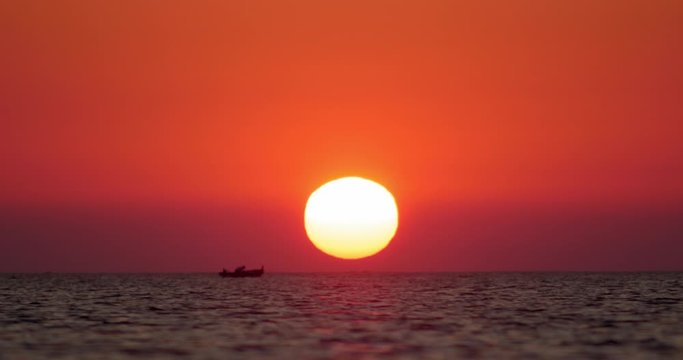 Huge sun during a beautiful sunset in front of the sea, boat passing by over the horizon