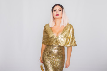 Charming young blonde haired woman wearing elegant gold evening dress and holding gold color clutch...
