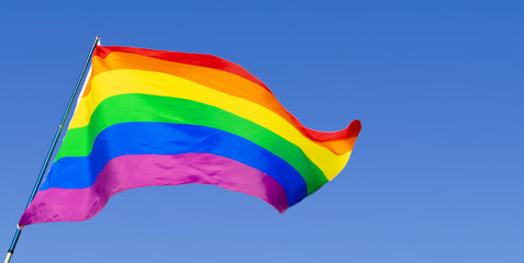 Gay rainbow flag waving in the wind in a clear blue sky