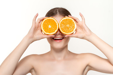 Close-up portrait of a happy beautiful young girl holding half of oranges close to face isolated over white background.