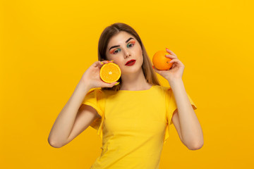 Close-up portrait of a beautiful young girl holding half of oranges close to face isolated over yellow background.