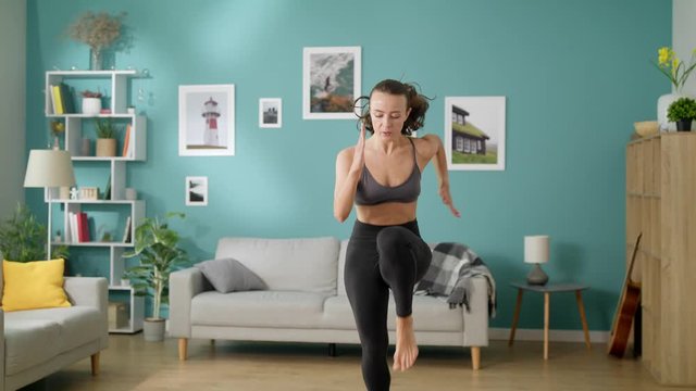 Beautiful slim woman does morning cardio exercises running on the spot in room