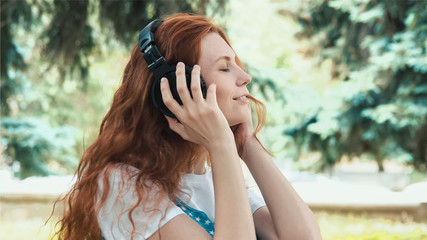 Ginger sensual girl dancing in park. Red-haired teenager walks in the park close-up. Young redhead woman on blurred green background. Freckled teenager outdoor.