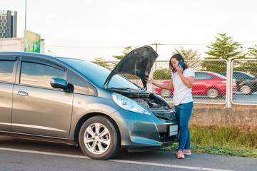 Asian teenage women holding a mobile phone Walking around the car, stressful mood during the evening hours. Along the highway Because her car broke down And she is waiting for help from someone.