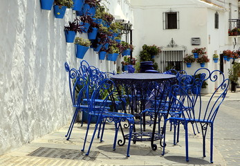 Fototapeta na wymiar Blue chairs and tables, next to traditional blue plant pots with Geraniums, attached to a white-washed wall, Spain