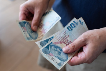 Hands of middle aged caucasian man counting 100 Turkish Lira bank notes in Izmir in Turkey.