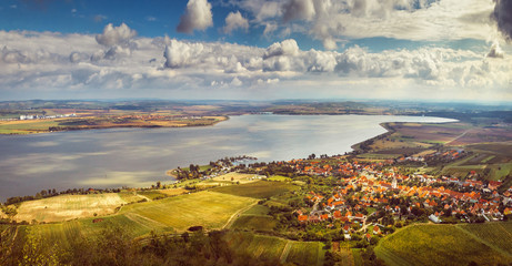 The Nové Mlýny Dam on the Dyje River.  Moravian village (Pavlov) with a dock at a large lake, around a vineyard, the sun illuminates the landscape in gold through white clouds in the blue sky