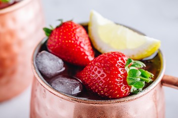 Refreshing iced Moscow mule alcoholic cocktail in copper mugs with strawberry and lemon