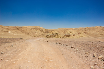 desert valley wasteland scenic landscape with ground trail for car through wilderness dunes to bare stone rocks and hills background