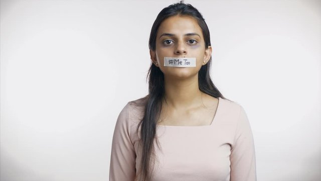 Female Indian victim of sexual harassment supporting me too movement - MeToo. Indian woman showing hashtag me too text on her taped mouth against sexual misconduct and violence - white background
