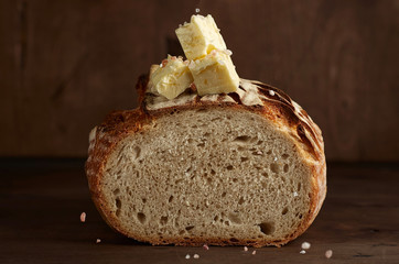 Artisan sourdough bread with butter and pink himalayan salt on dark wooden background