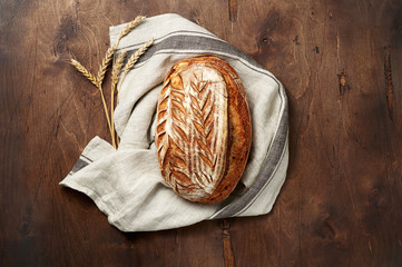Freshly baked Artisan sourdough bread loaves with wheat spike and kitchen towel on dark wooden background
