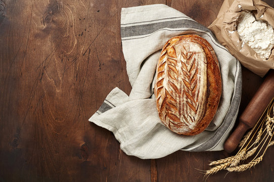 Freshly baked Artisan sourdough bread loaves with wheat spike and bag of flour on dark wooden background