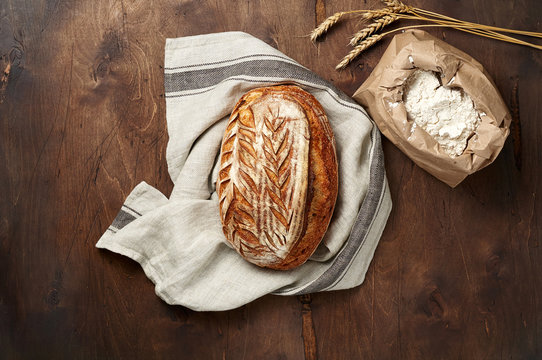 Freshly baked Artisan sourdough bread loaves with wheat spike and bag of flour on dark wooden background