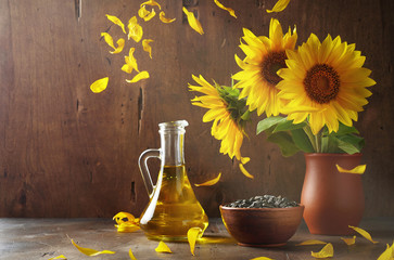 Still life of glass bottle with sunflower oil, seeds and flowers in ceramic vase