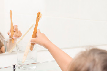A child in a bathroom puts a bamboo toothbrush in a glass. Zero waste concept.