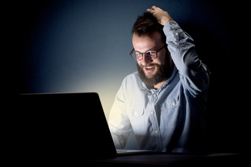 Young handsome businessman working late at night in the office with a dark background