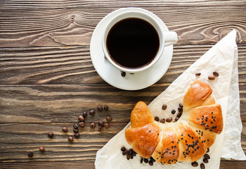 croissant, a cup of instant coffee and coffee beans on a textured wooden background top view, cozy and delicious breakfast. Rustic background