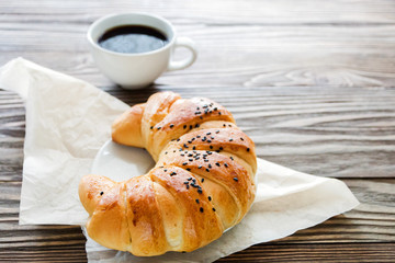 croissant and a cup of instant coffee on a textured wooden background top view, cozy and delicious breakfast. Rustic background
