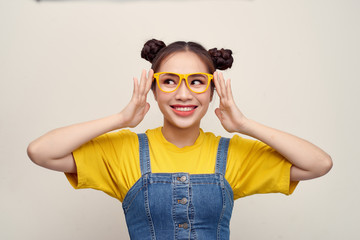 Beautiful Asian woman has two buns of hair wearing a jeans dungaree and adjusting glasses