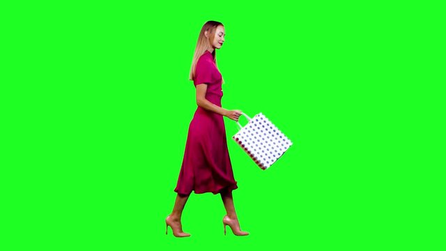 Cheerful shopper looking into her shopping bags and smiling happily while walking in full shot over green screen.