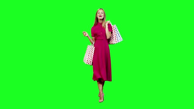 Excited stylish woman with her shopping bags, walking and smiling in full body shot over green screen.