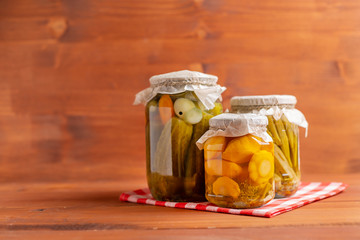 Jars of pickled vegetables: cucumbers, tomatoes, okra, eggplants on rustic wooden background.