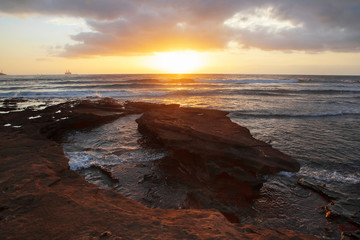 Tropical sunrise over the limestone coasts of El Medano, Tenerife, Canary Islands, Spain, beautiful seascape with vibrant colors overcast sky, golden haze light and dynamic waves striking rocky shores