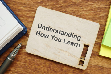 Writing note showing Understanding How You Learn. The text is written on a small wooden board with exclamation mark silhouette. Colored papers, pen, wooden background are on the photo too.
