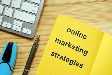 Writing note showing online marketing strategies.  The text is written in the yellow notebook. Keyboard, marker, pen, wooden background are on the photo.