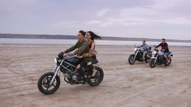 Group of young people riding motorbikes on the beach in evening. slow motion