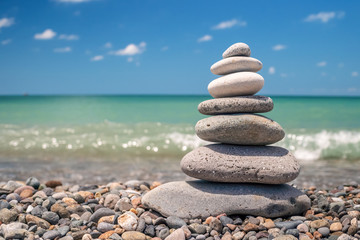 pyramid of sea pebbles on the beach against the backdrop of the sea wave in sunny day. concept of balance harmony and meditation. copy space