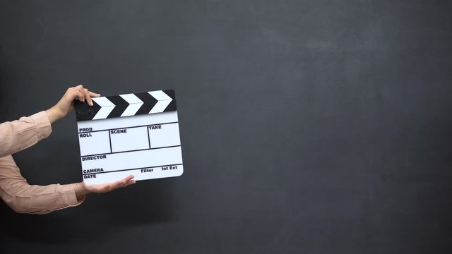 Female hands using clapperboard against black background, shooting movies