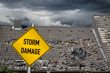 yellow damage warning sign in front of storm damaged roof of house